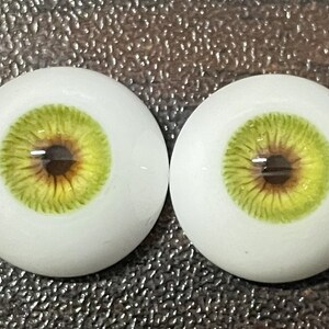 May include: Two realistic-looking green and brown doll eyes with a white sclera.