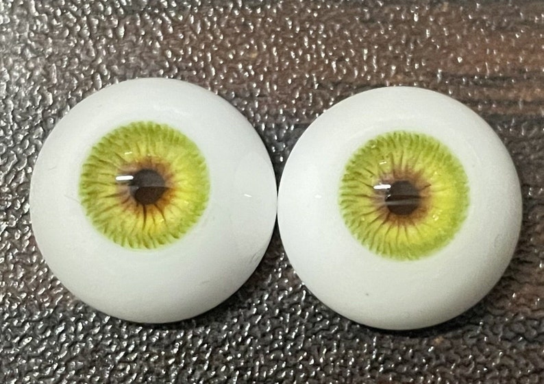 May include: Two realistic-looking green and brown doll eyes with a white sclera.