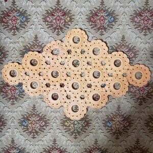 May include: A peach-colored crocheted doily with a diamond shape and a repeating pattern of circles. The doily is made with a delicate, openwork design.