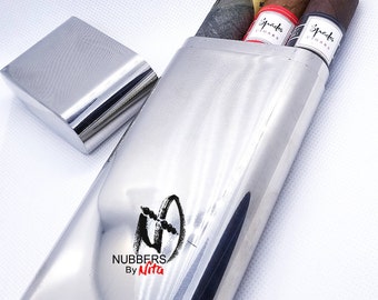 May include: A silver cigar case with two cigars inside. The cigars are wrapped in brown paper and have a red band with the word "Spades" on them. The case has the words "NUBBERS By Nita" printed on it.