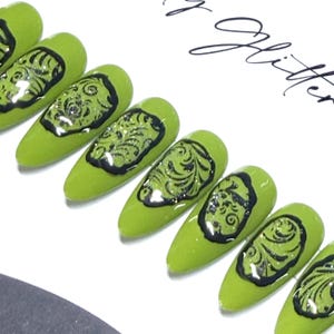 May include: A set of almond-shaped press-on nails featuring a glossy lime green base color. Each nail is decorated with a raised, black, swirling filigree pattern that creates a textured, embossed effect across the surface of the nail.