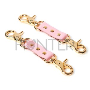 Könnte beinhalten: Zwei rosa Lederriemen mit goldenen Metallschließen und Nieten. Die Riemen sind etwa 7,5 cm lang.