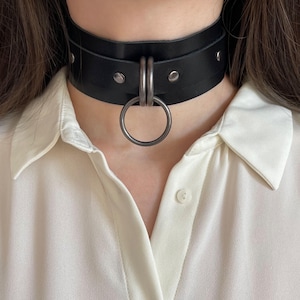 Close-up of a wide black leather collar with dark nickel hardware.
Front view.
