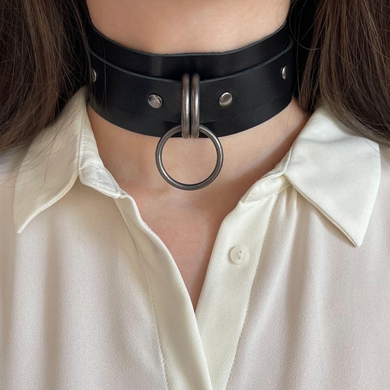 Close-up of a wide black leather collar with dark nickel hardware.
Front view.