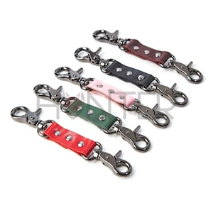 Könnte beinhalten: Fünf Leder-Schlüsselanhänger mit Metallschließen. Die Schlüsselanhänger sind in verschiedenen Farben: rot, grün, rosa, schwarz und braun.