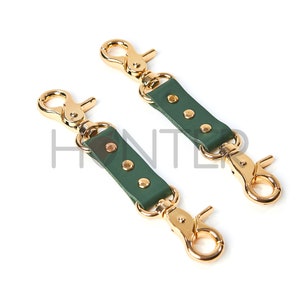 May include: Two gold-toned metal clasps with green leather straps and gold-toned rivets.