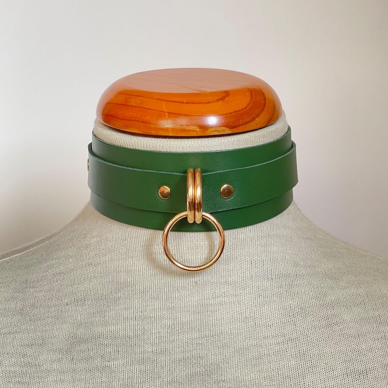 Close-up of a wide green leather collar with gold hardware.
Front view.