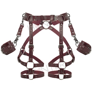 May include: Burgundy leather body harness with matching wrist cuffs. The harness features adjustable straps, metal rings, and silver-tone hardware. The cuffs attach with metal clasps. The design includes a belt, shoulder straps, and leg straps.