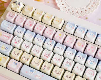 May include: A pastel-coloured keyboard with custom keycaps. The keycaps feature cat-themed designs and symbols, with a mix of pink, blue, and yellow hues. The keyboard has a white frame and a variety of function keys.