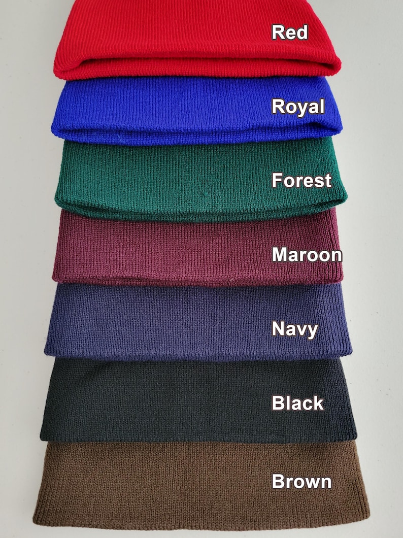 Op de afbeelding: Een stapel van acht gebreide mutsen in verschillende kleuren: rood, koninklijk blauw, bosgroen, donkerrood, marineblauw, zwart en bruin. De kleuren zijn op elke muts gelabeld.