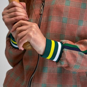 May include: A pink and green checked bomber jacket with a zip fastening and green, yellow and white striped cuffs.