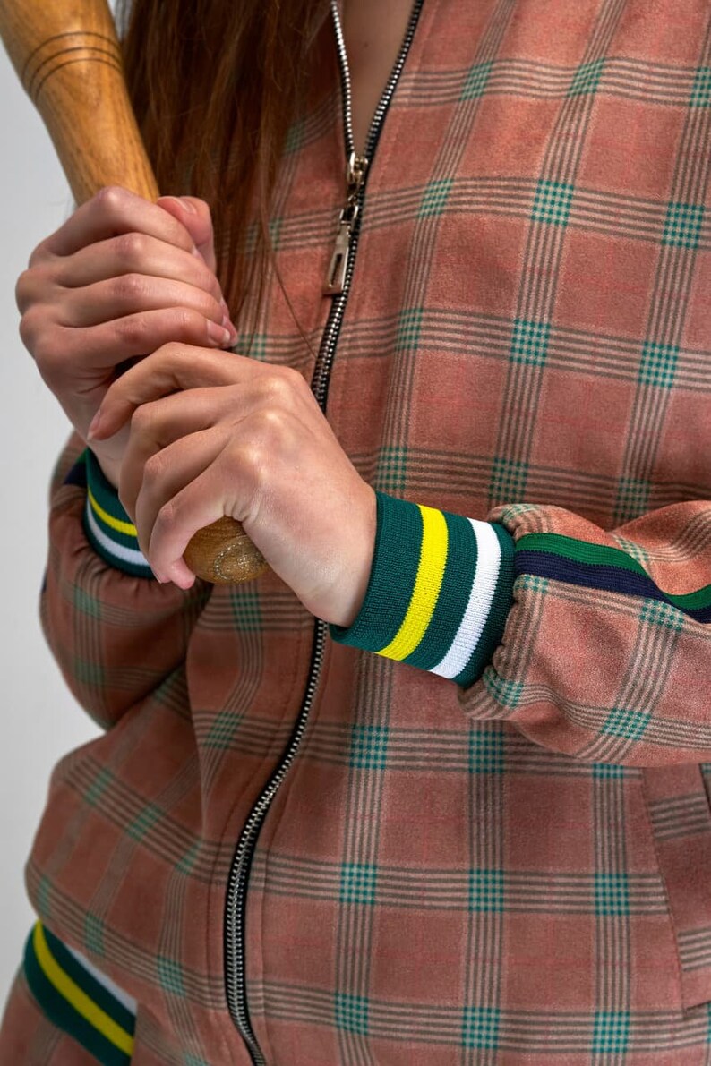 May include: A pink and green checked bomber jacket with a zip fastening and green, yellow and white striped cuffs.