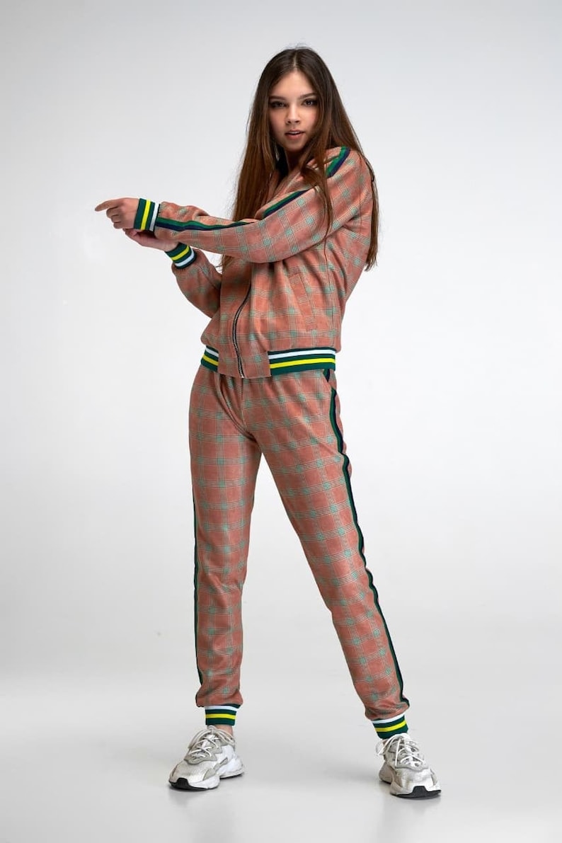 May include: A pink and green checked tracksuit with green and yellow trim. The jacket has a zip fastening and the trousers have a drawstring waist.