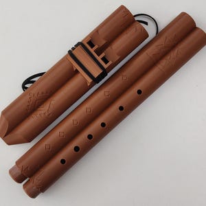 May include: A set of two brown wooden flutes with a decorative pattern. The flutes are joined together with a black cord.