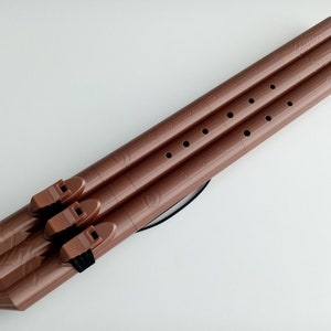 May include: A set of three brown wooden flutes with finger holes and a black strap. The flutes are connected together at the mouthpiece.