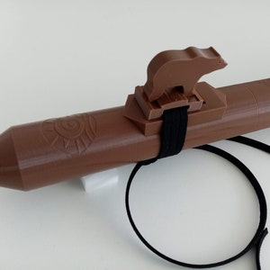 Puede incluir: Una flauta de madera marrón con una boquilla en forma de oso y una correa negra. La flauta tiene un diseño tallado en el cuerpo.