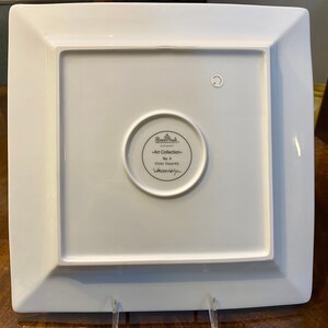 Puede incluir: Plato cuadrado de cer&aacute;mica blanca con un borde elevado y un logotipo circular en el centro. El logotipo dice "Rosenthal -Art Collection- No. 4 Versace"