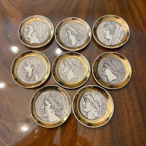 May include: Set of eight round ceramic coasters with gold trim. Each coaster features a black and white image of a historical figure's profile.