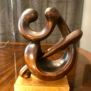 以下が含まれることがあります： 2つの絡み合った人物の彫刻。濃い茶色の仕上げで、明るい木製の台座が付いている。