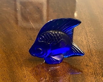 May include: A cobalt blue glass figurine of a fish. The fish has a stylized design with a large fin and a small eye.