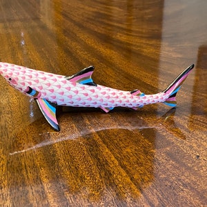 May include: A pink and black porcelain shark figurine with a geometric pattern. The shark has a long, slender body and a pointed snout.