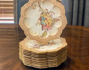 May include: A stack of 10 white porcelain plates with a gold rim and floral pattern. The top plate has a scalloped edge and a more detailed floral design.