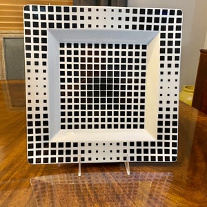 Puede incluir: Un plato cuadrado blanco para servir con un patr&oacute;n geom&eacute;trico en blanco y negro. El patr&oacute;n est&aacute; formado por peque&ntilde;os cuadrados.