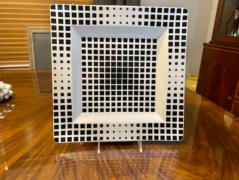 Puede incluir: Un plato cuadrado blanco para servir con un patr&oacute;n geom&eacute;trico en blanco y negro. El patr&oacute;n est&aacute; formado por peque&ntilde;os cuadrados.