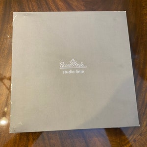 Puede incluir: Una caja gris con el texto "Rosenthal studio-linie" impreso en blanco.