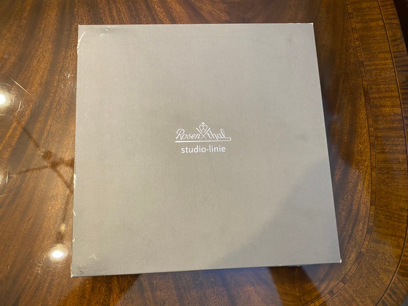 Puede incluir: Una caja gris con el texto "Rosenthal studio-linie" impreso en blanco.