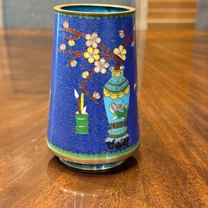Puede incluir: Un pequeño jarrón de cloisonné azul y dorado con un diseño floral. El jarrón está decorado con una rama de flores rosas y amarillas y un jarrón más pequeño con un diseño azul y blanco.