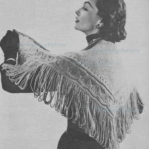 May include: A black and white photograph of a woman wearing a knitted shawl with fringe. The shawl features a delicate lace pattern and is draped over the woman's shoulders. The woman is looking down and has her hair styled in a short, curled bob.
