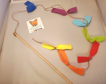 May include: A rainbow cat toy with a wooden stick. The toy has a string with felt pieces in different colors: blue, purple, light blue, green, orange, and red.