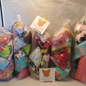 May include: Four bags of colorful catnip toys. Each bag contains several small, triangular-shaped toys made of fabric with different patterns. The toys are packaged in clear plastic bags with a yellow twist tie. The bags are labeled with the text "Cheeky Cat Creations Handmade Catnip Toys".