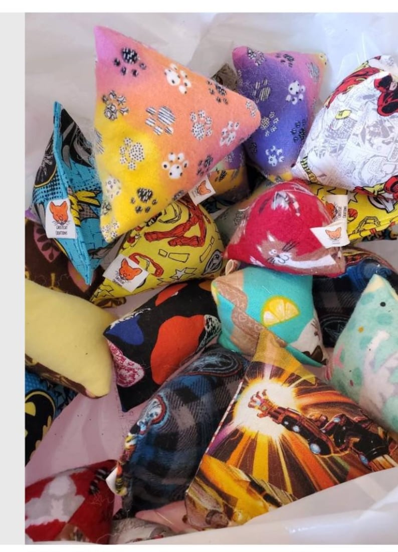 Puede incluir: Una colecci&oacute;n de coloridos juguetes triangulares para gatos. Los juguetes presentan varios patrones, incluyendo huellas de patas, personajes de c&oacute;mics y dise&ntilde;os abstractos. Cada juguete tiene una peque&ntilde;a etiqueta con un logotipo de zorro.