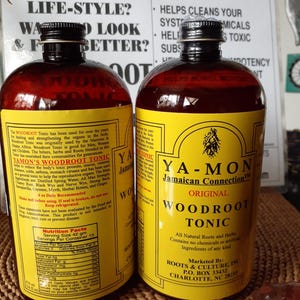 Puede incluir: Dos botellas de Ya-Mon Jamaican Connection Original Woodroot Tonic. Las botellas tienen etiquetas amarillas con texto negro y un l&iacute;quido marr&oacute;n en el interior. Las etiquetas enumeran los ingredientes e instrucciones. El fondo incluye texto sobre la mejora del estilo de vida.