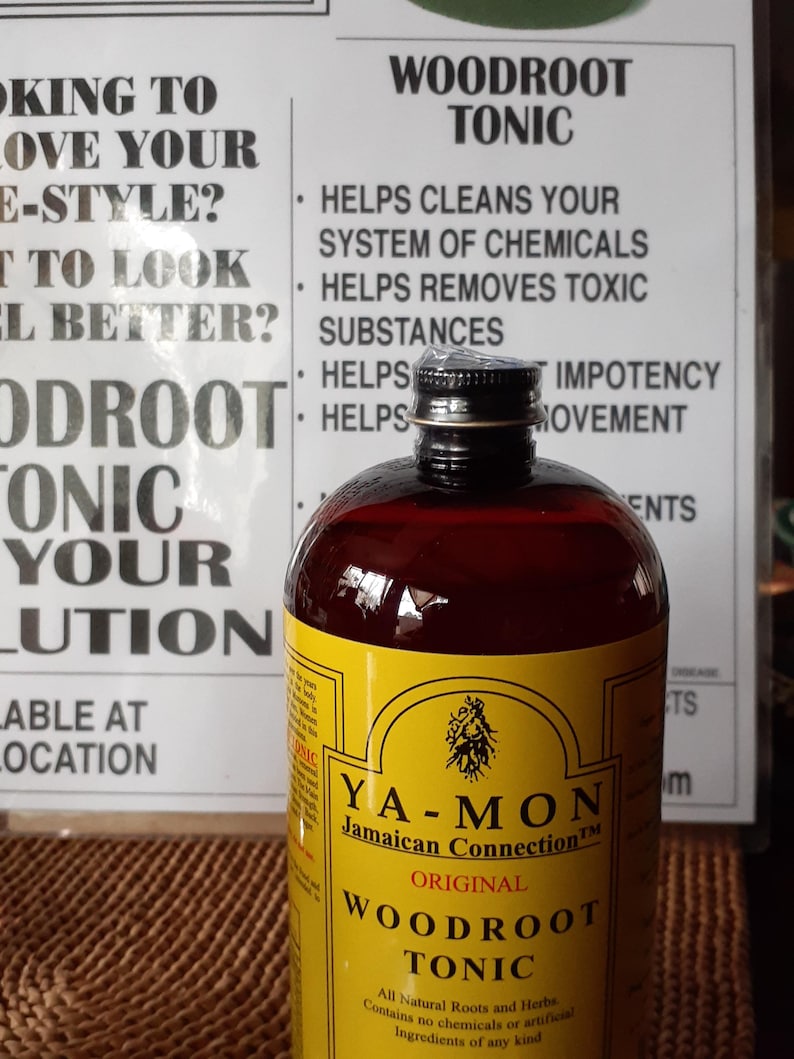 Puede incluir: Una botella de Ya-Mon Jamaican Connection Woodroot Tonic con una etiqueta amarilla y l&iacute;quido oscuro. La etiqueta incluye texto sobre los ingredientes y beneficios del producto. La botella est&aacute; frente a un letrero con texto sobre el t&oacute;nico.