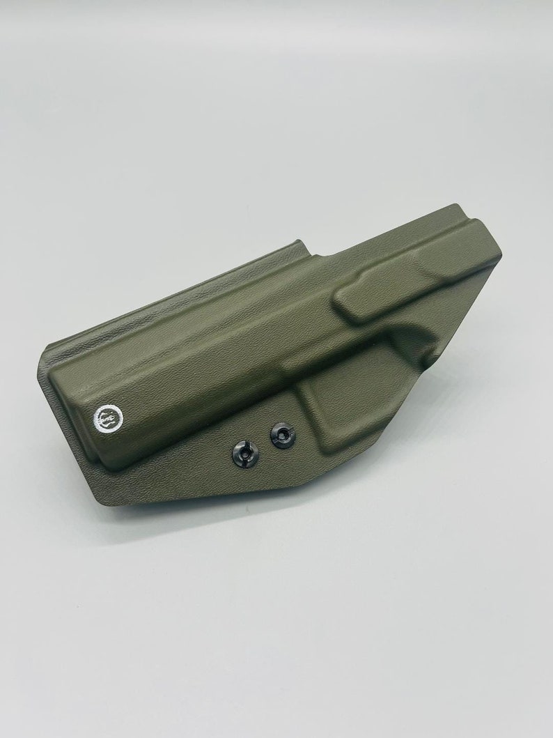 May include: A green, molded plastic holster for a firearm. The holster has two black screws on the bottom and a white circle logo on the side.