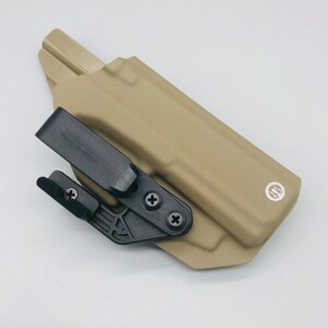 May include: A tan leather holster with a black clip and a black adjustment lever. The holster has a small, round logo on the side.