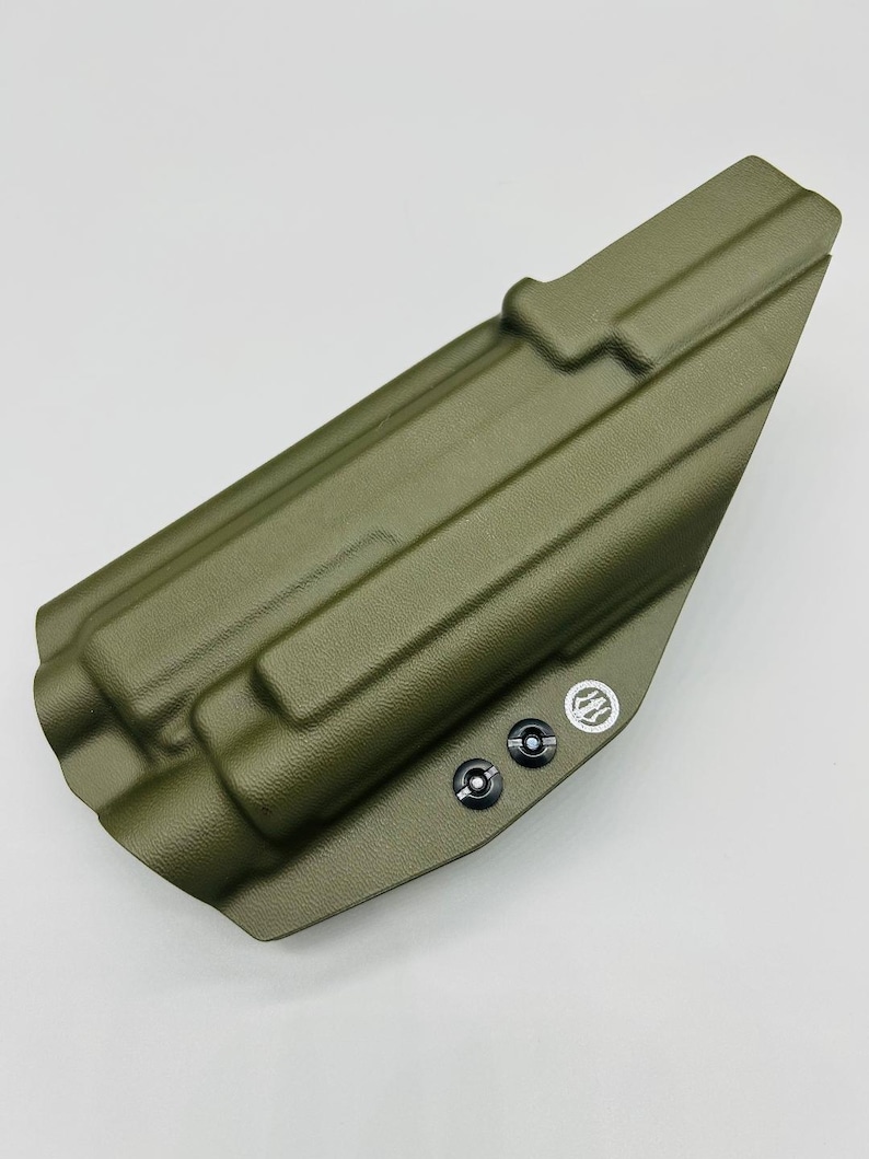 May include: A green, textured, molded plastic holster with two black screws and a logo. The holster is designed to hold a firearm.