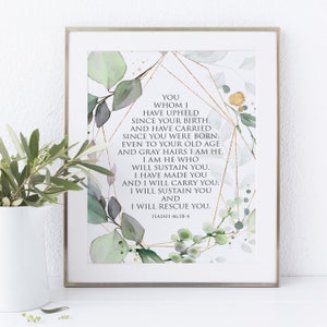 May include: A framed print with a gold geometric design and green watercolour leaves. The print features a bible verse from Isaiah 46:3-4, "You whom I have upheld since your birth, and have carried since you were born. Even to your old age and gray hairs I am He. I am He who will sustain you. I have made you and I will carry you; I will sustain you and I will rescue you."