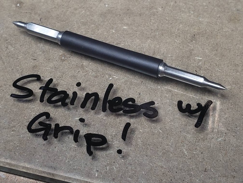 May include: A close-up of a black and silver tool with a pointed tip. The tool has a black rubber grip and the text "Stainless w Grip!" is written on the surface below the tool.