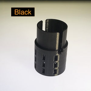 May include: Black plastic 3D printed object with a cylindrical shape and a series of holes around the middle.