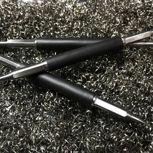 May include: Three black and silver metal tools with pointed tips, lying on a bed of silver metal shavings.