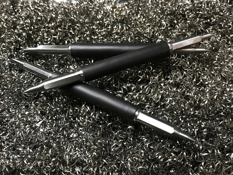 May include: Three black and silver metal tools with pointed tips, lying on a bed of silver metal shavings.
