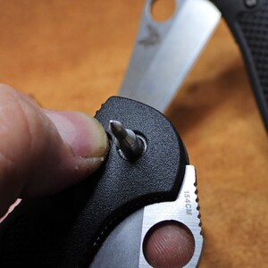 May include: A black folding knife with a silver blade and a small screwdriver tool. The knife is partially open and the screwdriver is extended. The knife has a black handle with a textured grip and the blade has a 15.4CM marking.
