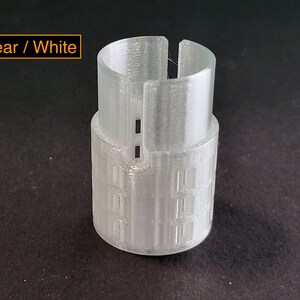 May include: A clear white plastic tube with a textured surface and a small opening at the top. The tube has a series of horizontal lines around the middle.