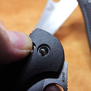 May include: Close-up of a black pocket knife with a silver blade. The knife has a black plastic handle with a small silver screw visible. The blade is partially open and the text "154CM" is visible on the blade.
