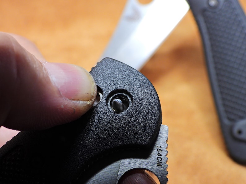 May include: Close-up of a black pocket knife with a silver blade. The knife has a black plastic handle with a small silver screw visible. The blade is partially open and the text "154CM" is visible on the blade.