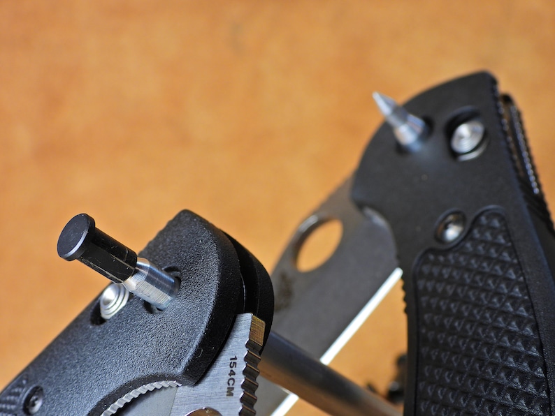May include: Close-up of a black knife sharpener with a silver metal rod and a black handle. The sharpener has a small silver screw and the text "15.4CM" is printed on the side.